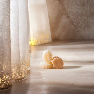 Fondants parfumés au musc égyptien disposés sur un sol lumineux près de rideaux, créant une ambiance cocooning et raffinée pour la maison